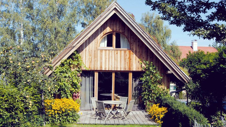 Ein gem&uuml;tliches Holzferienhaus mit Terrasse, umgeben von B&auml;umen und Blumen.