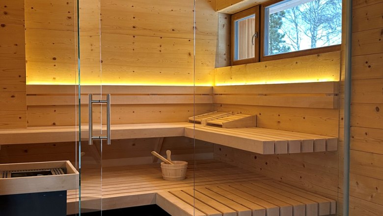 Innenansicht einer modernen Sauna mit Holzbänken und Glaswand.