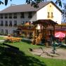 Ein Gasthof mit Spielplatz im Vordergrund, umgeben von gr&uuml;ner Wiese und B&auml;umen.
