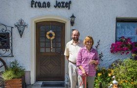 Ein Paar steht vor dem G&auml;stehaus Frans Jozef mit einem Hund auf dem Gehweg.