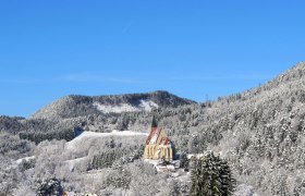 Winterlandschaft mit Kirche in verschneiten Bergen unter blauem Himmel.