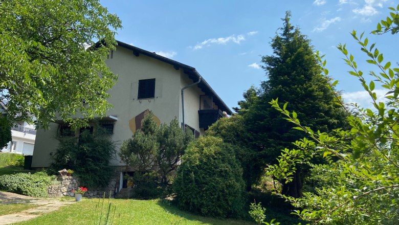 Ein zweist&ouml;ckiges Haus mit Garten und B&auml;umen, bei sonnigem Wetter.