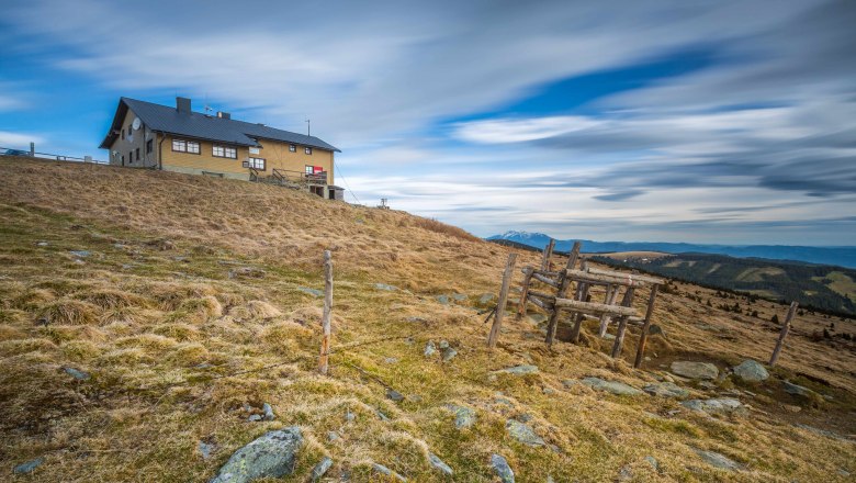 Ein Berghaus auf einer grasbewachsenen Anh&ouml;he unter einem bew&ouml;lkten Himmel.