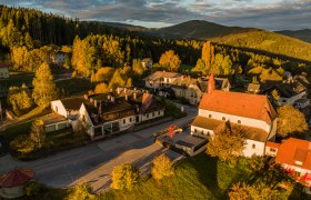 Luftaufnahme von St. Corona am Wechsel mit Kirche und umliegenden Geb&auml;uden in herbstlicher Landschaft.