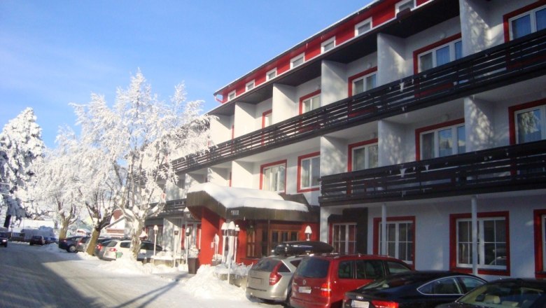Winterliches Hotel mit verschneiten Bäumen und parkenden Autos.