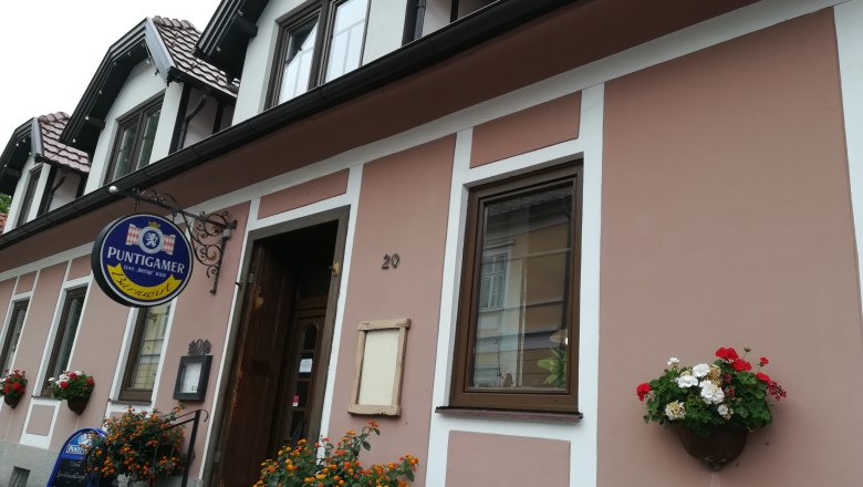 Außenansicht eines Gebäudes mit Schild 'Puntigamer' und Blumendekoration.