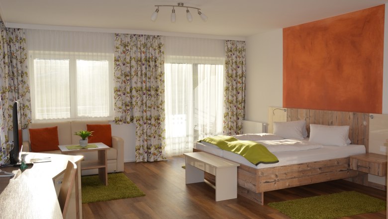 Ein modernes Doppelzimmer mit Holzboden, einem Doppelbett, Sofa, Tisch und großen Fenstern mit Vorhängen.