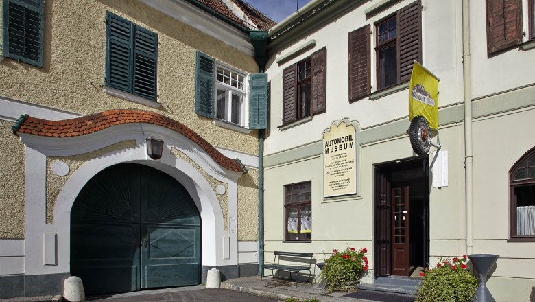 Eingang des Automobilmuseums Aspang Markt mit gelber Fahne und Blumen.