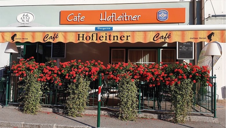Außenansicht des Café Hofleitner mit roten Blumen und Markise.