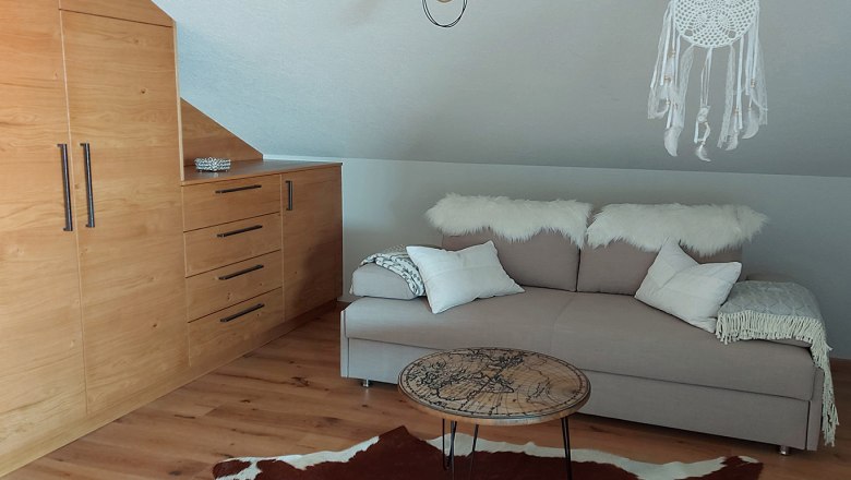 Gemütliches Zimmer mit Ausziehcouch, Holzmöbeln und Traumfänger.