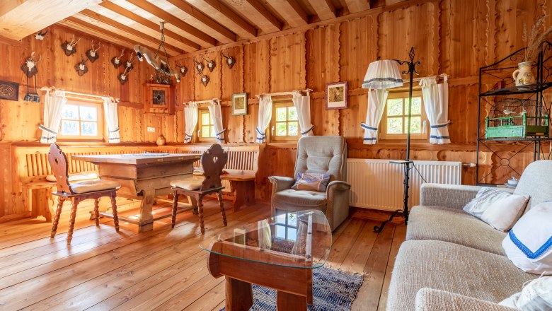 Rustikaler Wohn- und Essbereich mit Holzmöbeln, Holzwänden und Jagdtrophäen an der Wand.