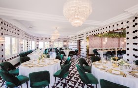 Elegantes Restaurant mit runden Tischen, grünen Stühlen und Kronleuchtern.