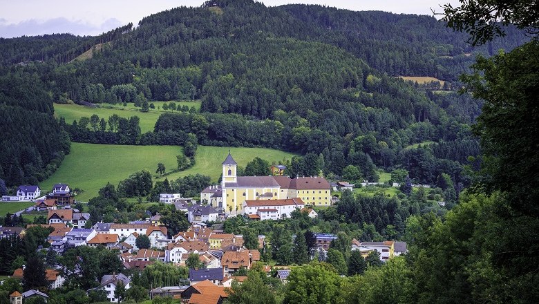 Eine Kirche thront &uuml;ber einem malerischen Dorf, umgeben von gr&uuml;nen H&uuml;geln und W&auml;ldern.
