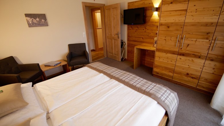 Schlafzimmer mit Doppelbett, Holzmöbeln und Fernseher an der Wand.