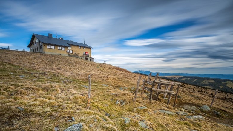 Bergh&uuml;tte auf einem H&uuml;gel mit bew&ouml;lktem Himmel im Hintergrund.