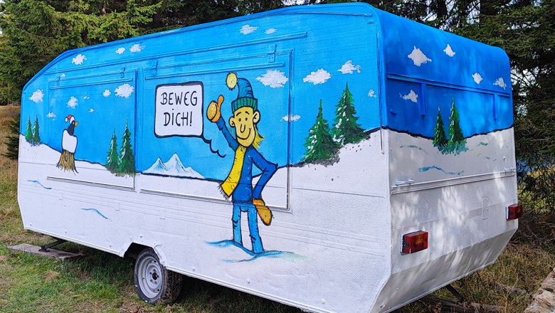 Ein bunt bemalter Wohnwagen mit einer Winterlandschaft und einer Figur, die "Beweg dich!" sagt.