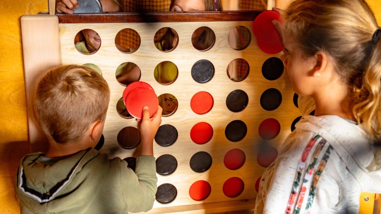 Kinder spielen ein gro&szlig;es Vier-Gewinnt-Spiel mit roten und schwarzen Scheiben.