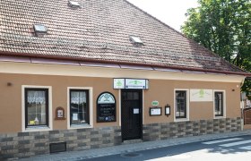 Historisches Gebäude mit brauner Fassade und Schildern. Es hat ein Ziegeldach und Fenster mit Gardinen.