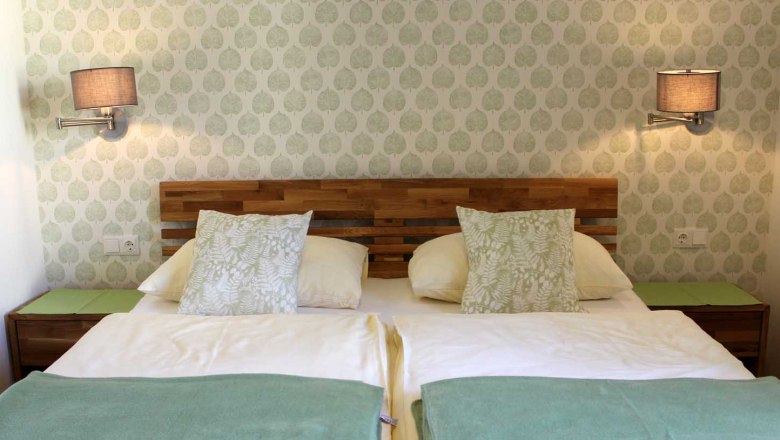 Gemütliches Zimmer mit Doppelbett, Mustertapete, Wandlampen, Nachttischen und Kissen.