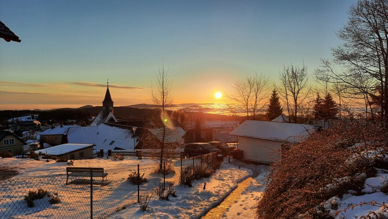 Winterlicher Sonnenaufgang über einer verschneiten Landschaft mit Kirche und Häusern.