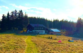 Ein Bauernhaus auf einer Wiese, umgeben von B&auml;umen und unter einem blauen Himmel.