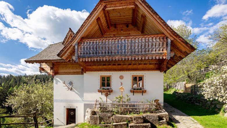 Traditionelles Haus mit Holzbalkon und wei&szlig;er Fassade, umgeben von Natur.