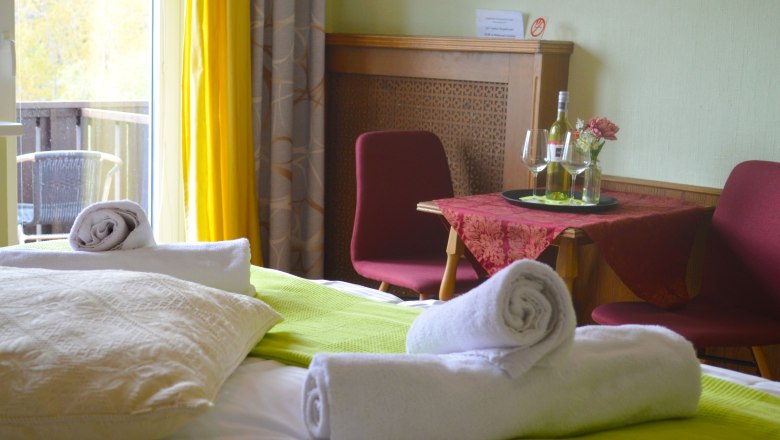 Doppelzimmer mit Bett, Tisch, St&uuml;hlen und Balkon.