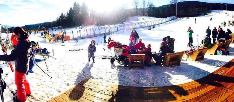 Winterlandschaft mit Menschen beim Skifahren und Entspannen auf Bänken im Schnee.