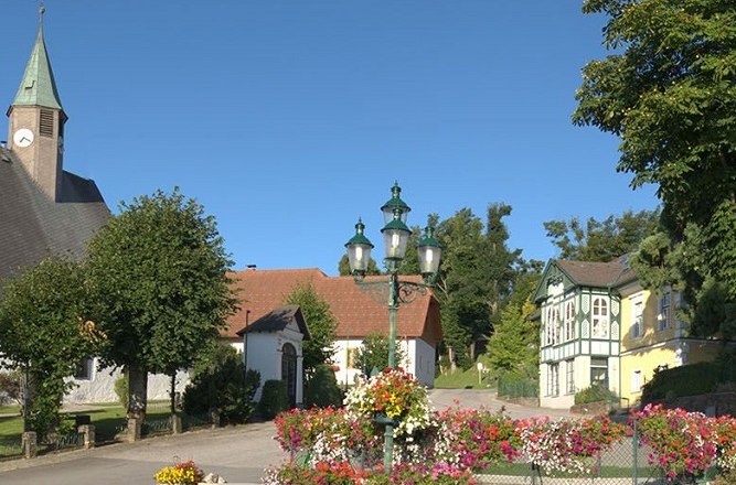 Hauptplatz in M&ouml;nichkirchen mit Kirche, Blumen und historischen Geb&auml;uden.
