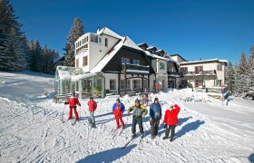 Winterliche Szene mit Alpengasthof Enzian und Skifahrern im Schnee.