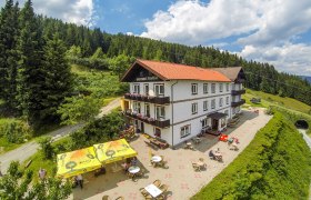 Alpengasthof mit Terrasse und Sonnenschirmen in bergiger Landschaft.