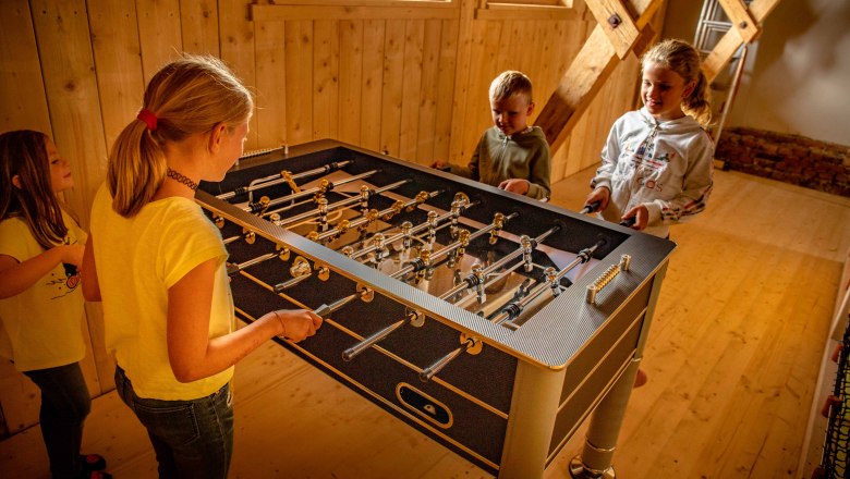 Kinder spielen Tischfu&szlig;ball in einem Holzraum.