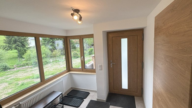 Heller Vorraum mit gro&szlig;en Fenstern, Holzt&uuml;r und Fliesenboden.