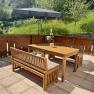 Holzterrasse mit Tisch, B&auml;nken und Sonnenschirm, umgeben von gr&uuml;nem Garten.