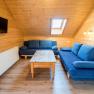Wohnzimmer mit Holzwänden, blauen Sofas, Holztisch und Dachfenster.