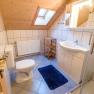Badezimmer mit Dachschräge, Waschbecken, Toilette, Dusche und blauem Teppich.