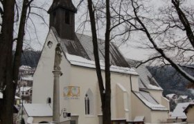 Eine Kirche im Winter mit schneebedecktem Boden und kahlen B&auml;umen.