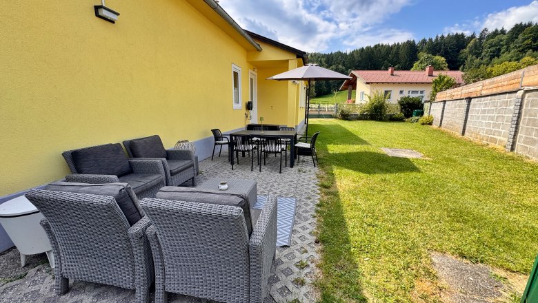 Terrasse mit Gartenm&ouml;beln und Sonnenschirm neben gelbem Haus.