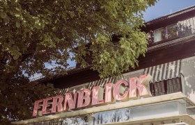 Geb&auml;ude mit dem Schriftzug 'FERNBLICK' und B&auml;umen im Vordergrund.