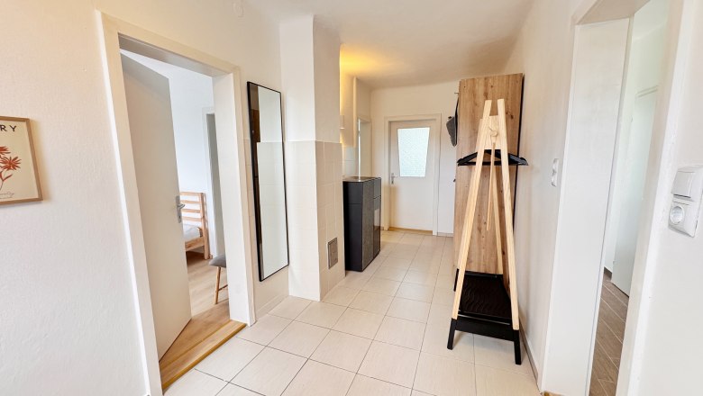 Heller Flur mit Fliesenboden, Spiegel, Garderobe und T&uuml;ren zu angrenzenden R&auml;umen.