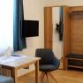 Modernes Gästezimmer mit Tisch, Stuhl, Kleiderschrank, Sofa, Fernseher und blauen Vorhängen.
