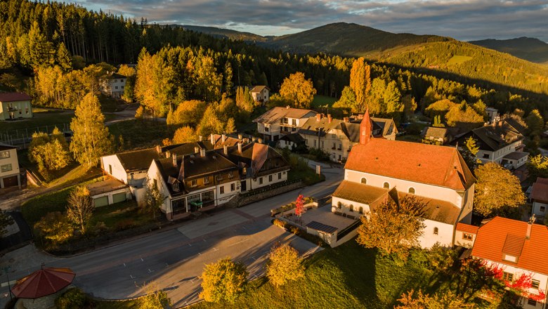 Luftaufnahme von St. Corona am Wechsel mit Kirche und umliegenden Geb&auml;uden in herbstlicher Landschaft.
