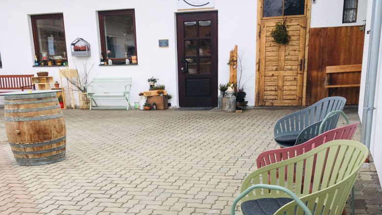 Sitzbereich vor einem Kaufhaus mit bunten St&uuml;hlen und einem Fass.