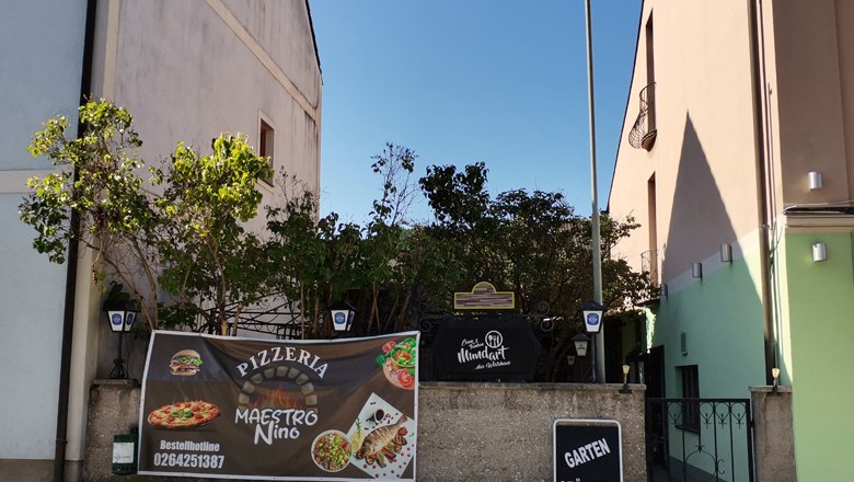 Eingang einer Pizzeria mit Werbebanner und Schild 'Garten geöffnet'.