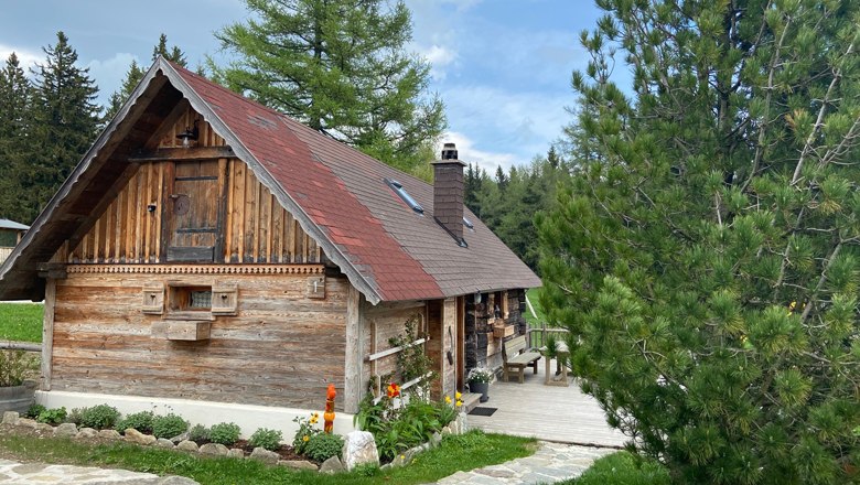 Eine rustikale Holzhütte mit rotem Dach in einer bewaldeten Umgebung, umgeben von Bäumen und einem gepflegten Garten.