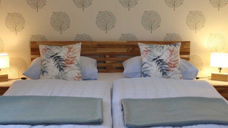 Gemütliches Doppelbett mit Holzkopfteil, Decken und Kissen und Nachttischen mit Lampen.