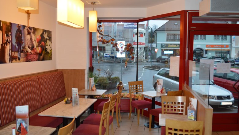 Innenansicht eines gem&uuml;tlichen Caf&eacute;s mit roten St&uuml;hlen und Tischen, Blick auf eine Stra&szlig;e durch gro&szlig;e Fenster.