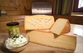 Verschiedene K&auml;sesorten auf einem Holzbrett mit einem Glas eingelegtem K&auml;se und einer Sch&uuml;ssel Frischk&auml;se.