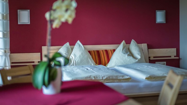 Gem&uuml;tliches Schlafzimmer mit roter Wand, Holzbett und Kissen.