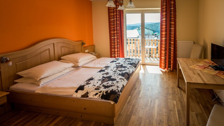 Gemütliches Hotelzimmer mit Doppelbett, Holzmöbeln und Balkon mit Ausblick.
